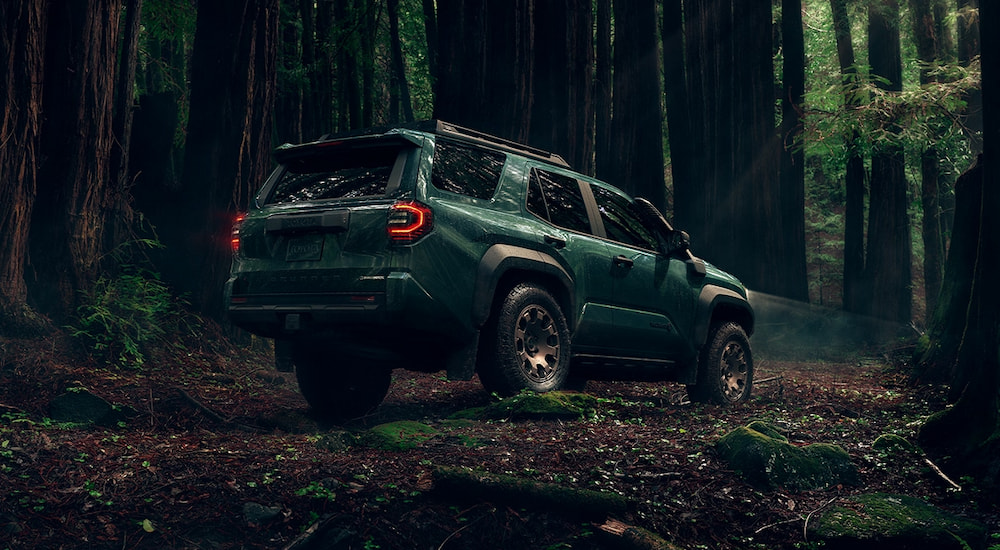 Rear of a dark green 2026 Toyota 4Runner Trailhunter parked off-road in a forest.