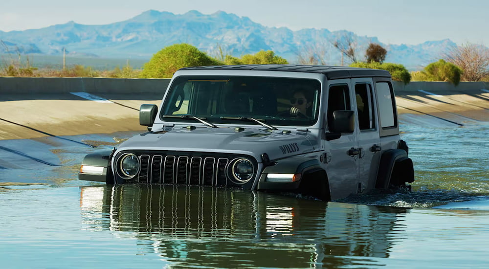 Grey 2026 Jeep Wrangler driving through a shallow canal.