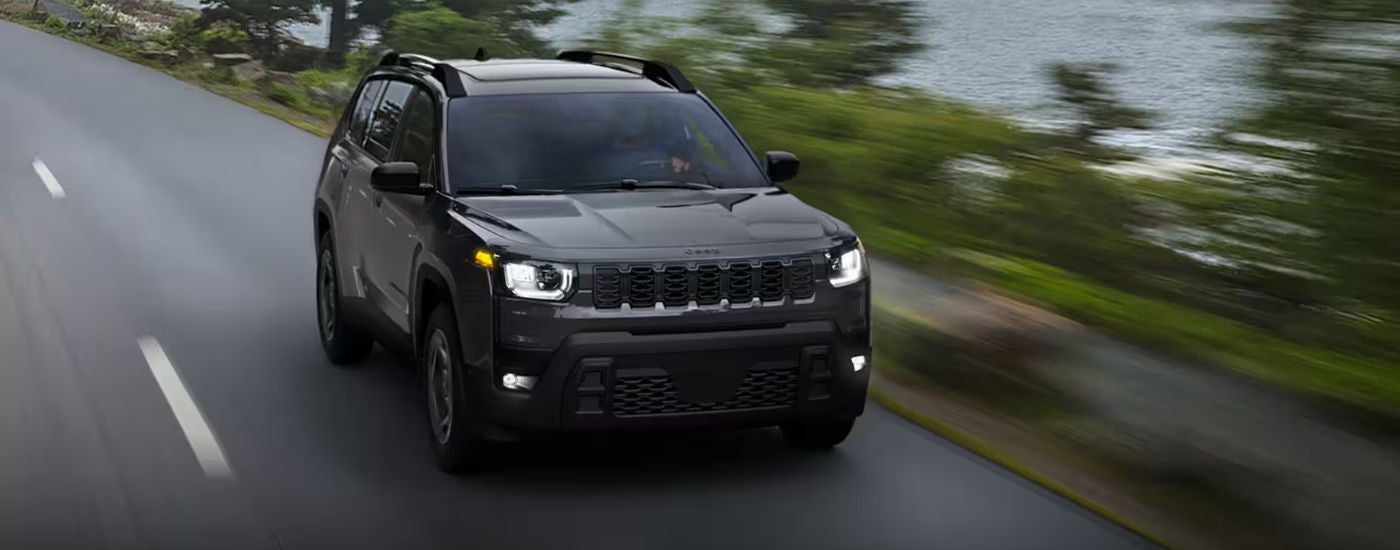 Black 2026 Jeep Cherokee Limited driving on a paved road.