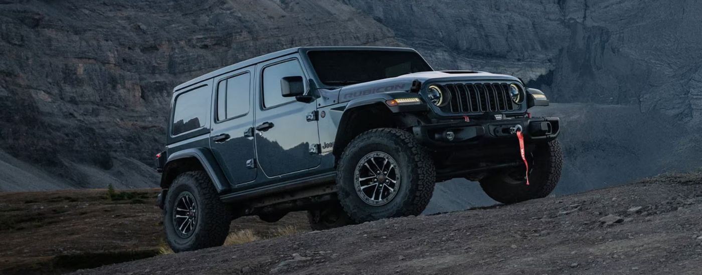 Blue 2026 Jeep Wrangler driving up a rocky hill.