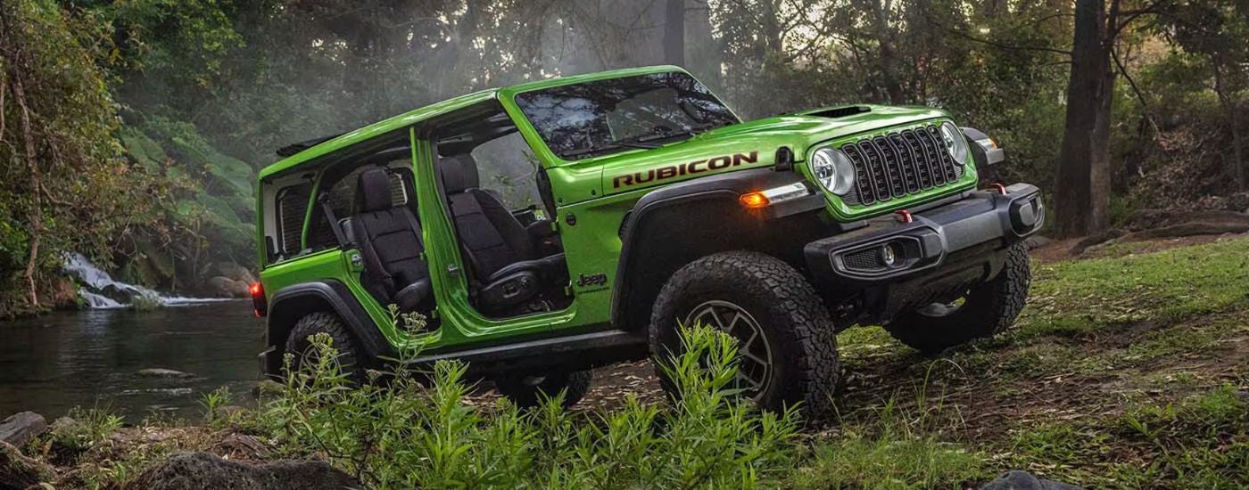 Green 2026 Jeep Wrangler Rubicon in the forest by a river.