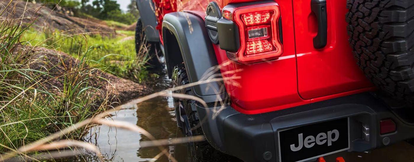 Red 2026 Jeep Wrangler close up of the rear while driving through a puddle.