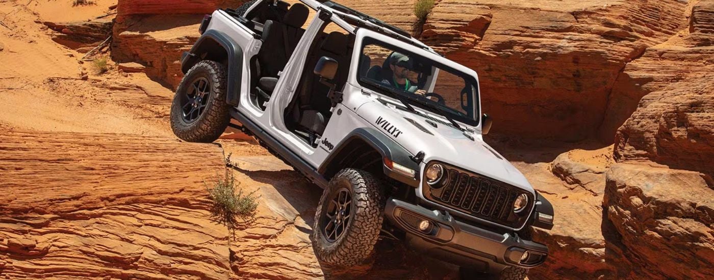 White 2026 Jeep Wrangler driving down a rocky desert hill.
