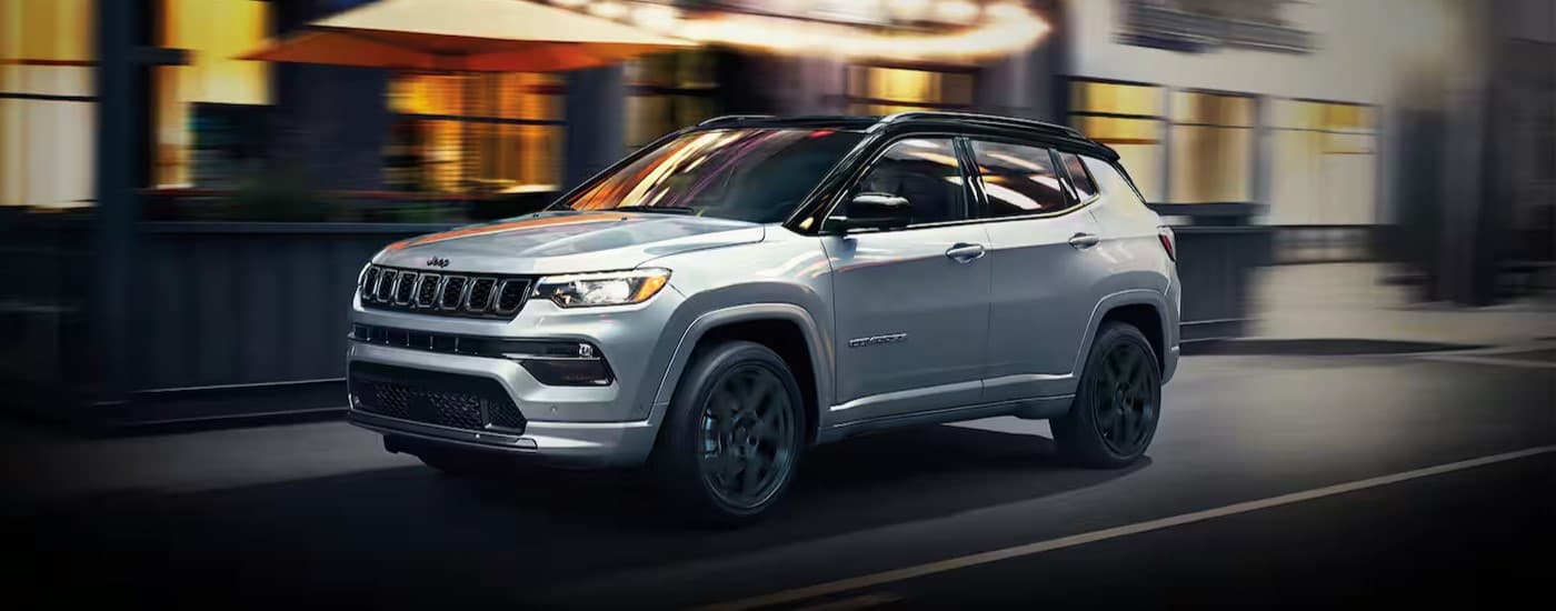 A silver 2024 Jeep Compass driving in a city.