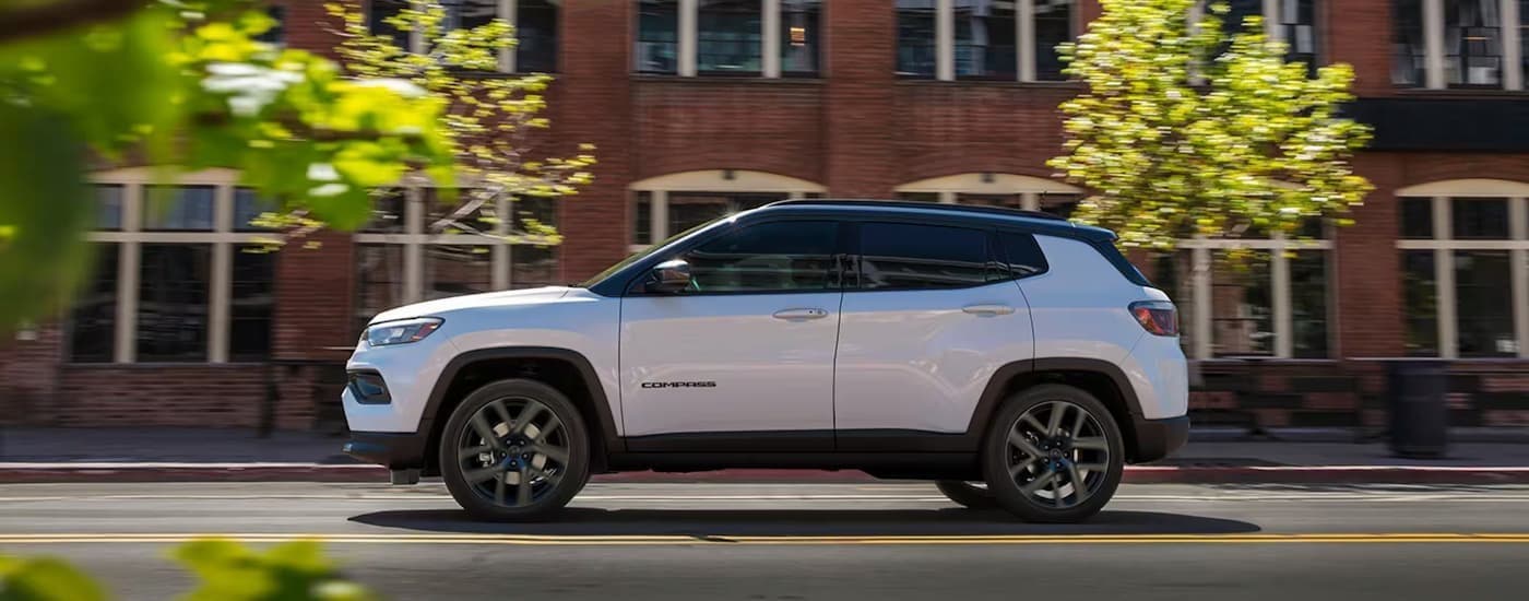 A white 2026 Jeep Compass for sale driving in a city.